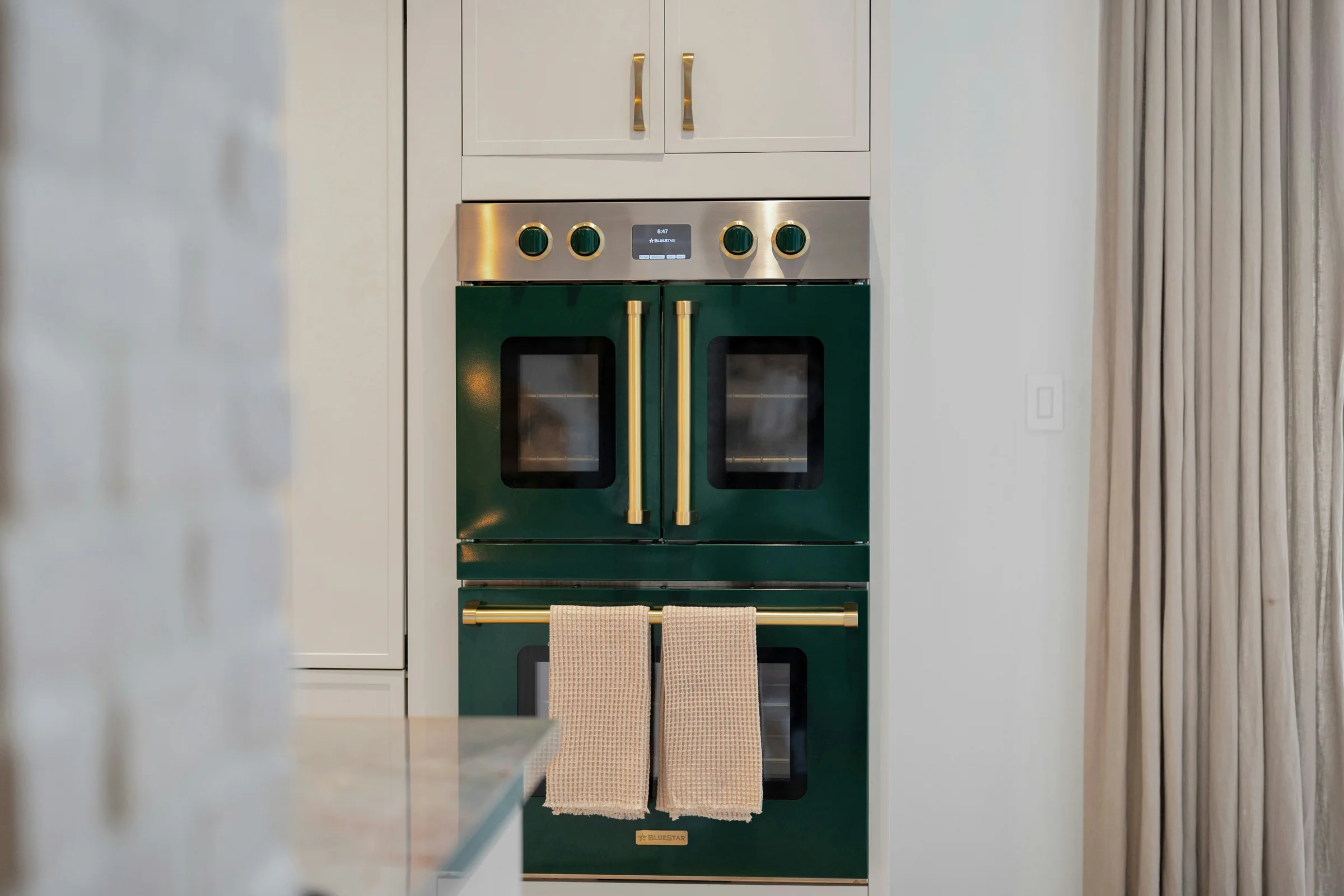 Green double oven set within light kitchen cabinetry