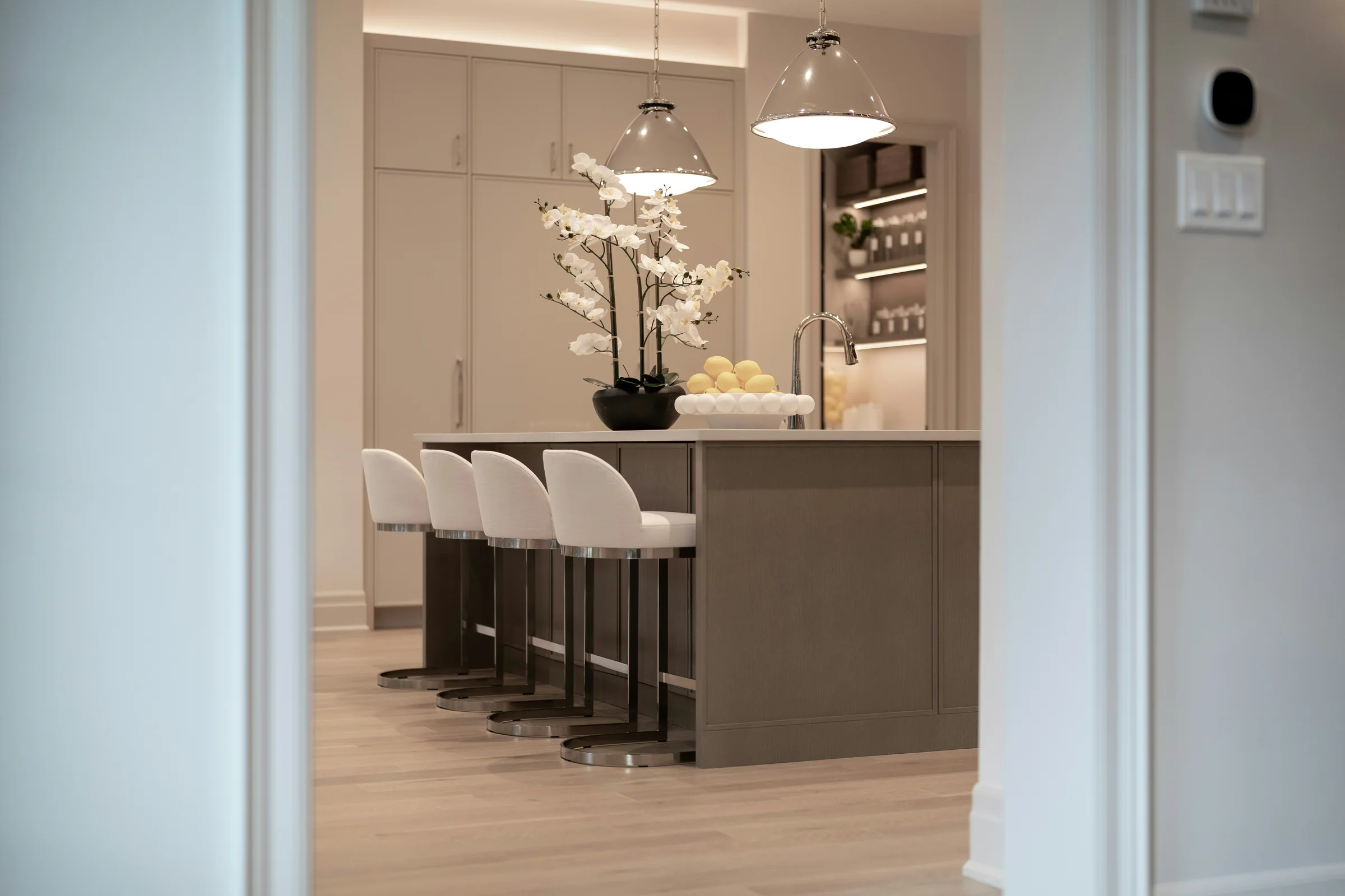 View through a doorway to an island with white upholstered stools