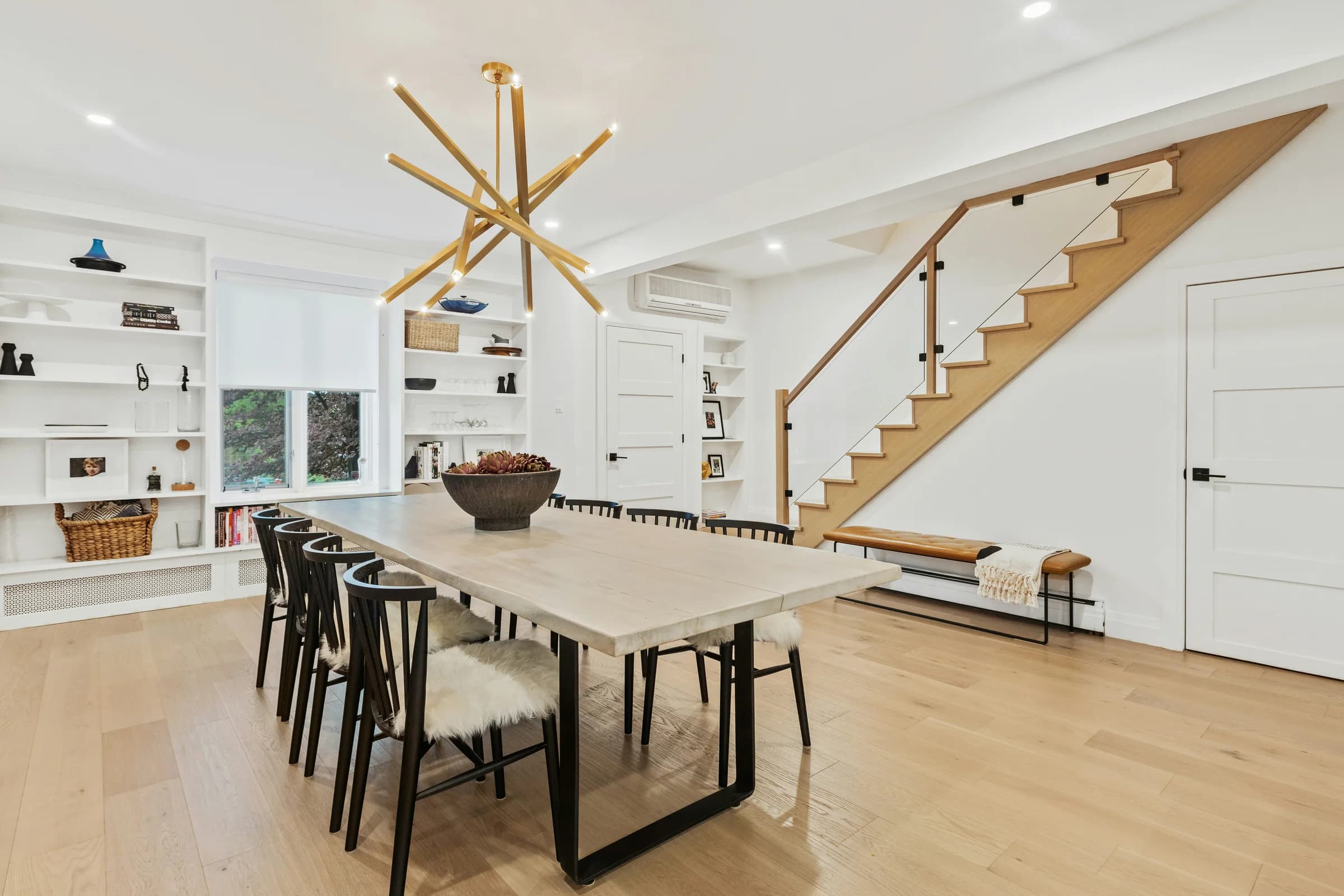 Open dining room with a sculptural brass pendant and oak staircase