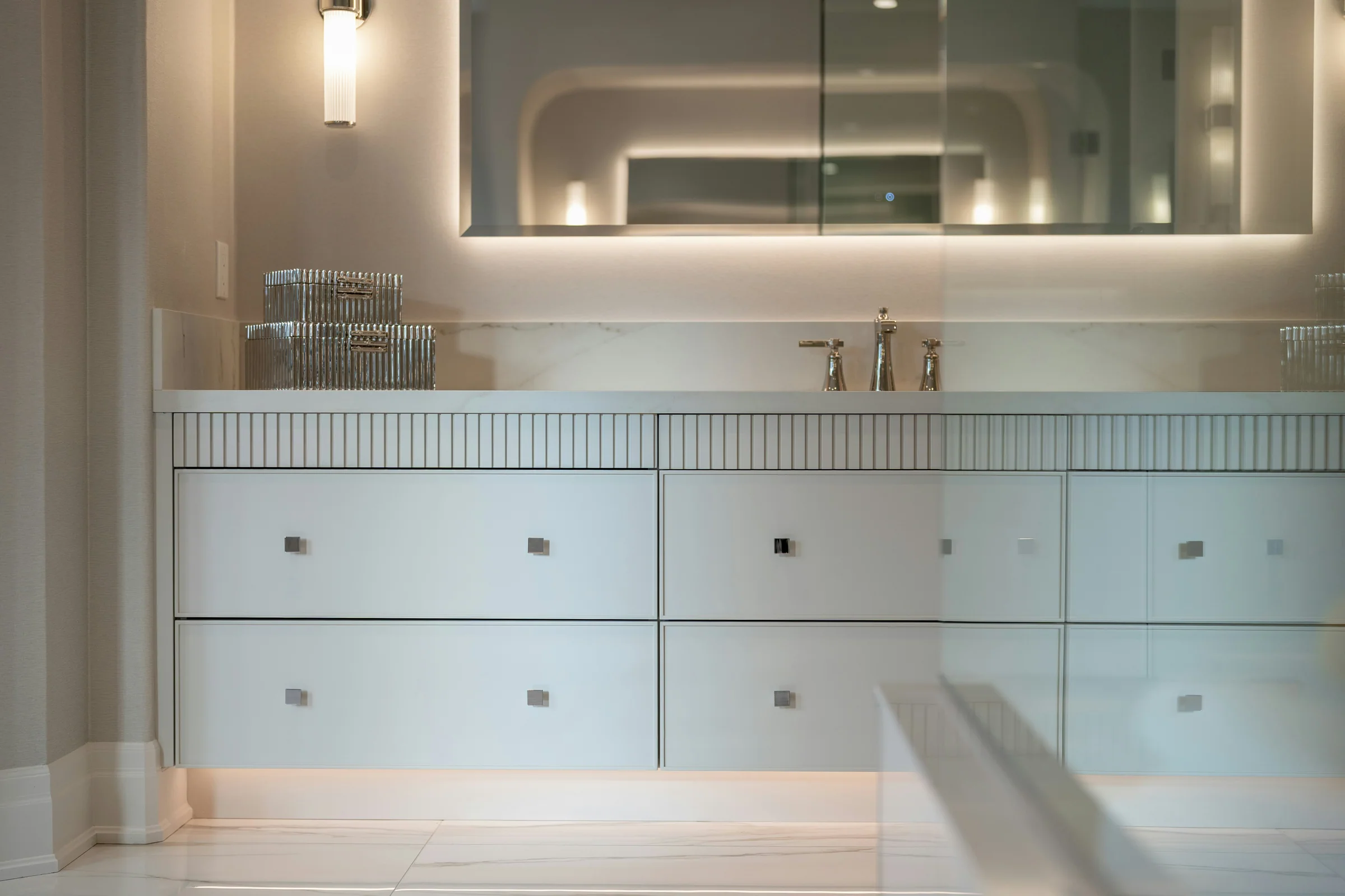 Pale bathroom vanity with ribbed drawer details and brass fittings
